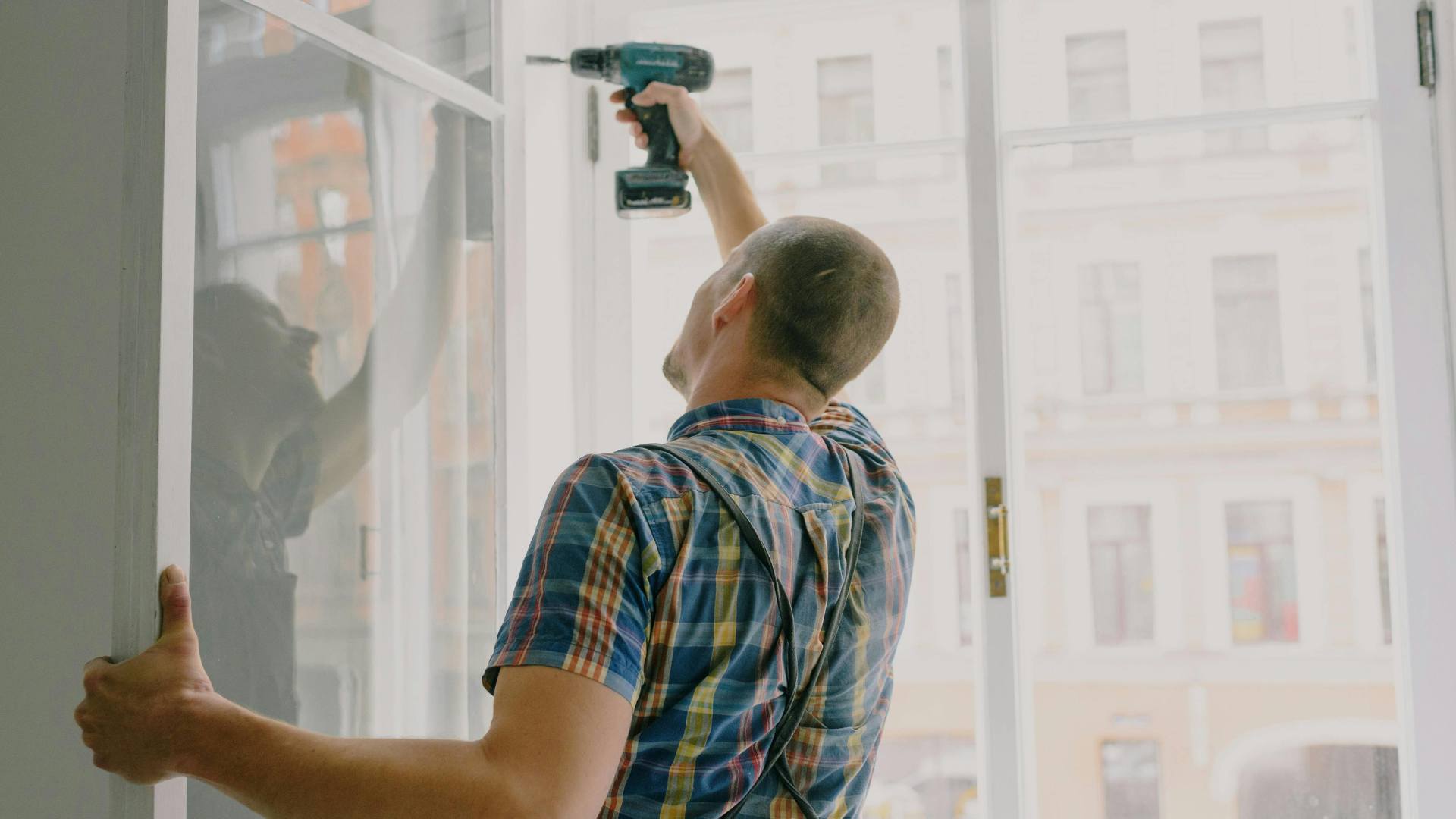Installer securing a glass window frame with a drill